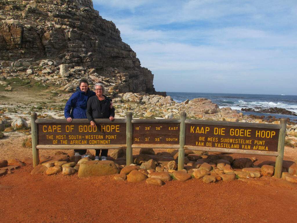 Photographic Safaris South Africa Tourists at Cape of Good Hope sign with rocky coastline in background.