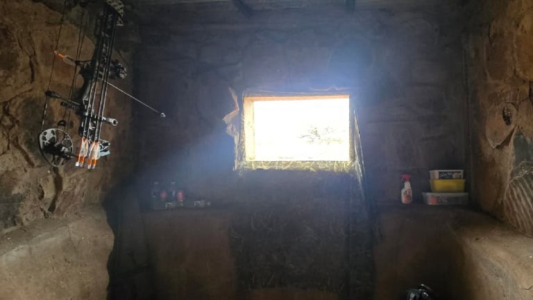Traditional hunting blind with a window and hunting equipment inside.