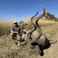 Hunter with bow and antelope trophy in open grassland.