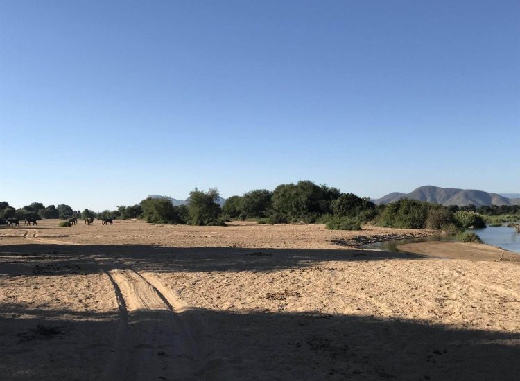 Zimbabwe Hunting Scenic African landscape with river, trees, and mountains under a clear blue sky.