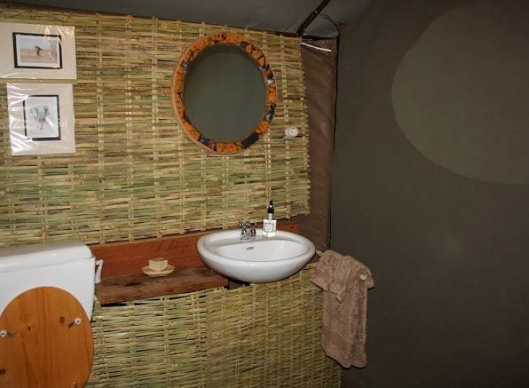 Mozambique Hunting Bathroom with bamboo wall, mirror, sink, and wooden accents.