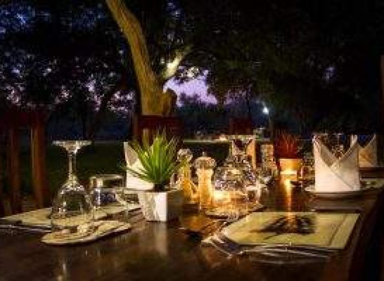 Zimbabwe Hunting Elegant outdoor dining setup with candles and tableware at sunset.