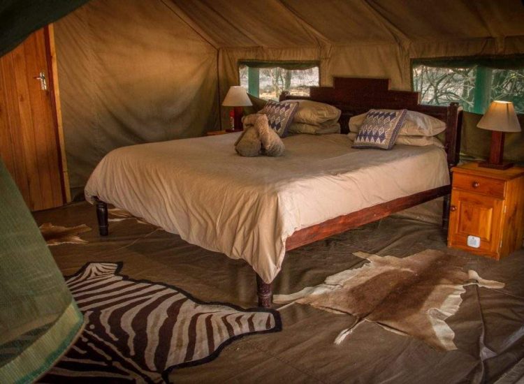 Zimbabwe Hunting Elegant safari tent bedroom with cozy bed, wooden furniture, and animal hide rug.